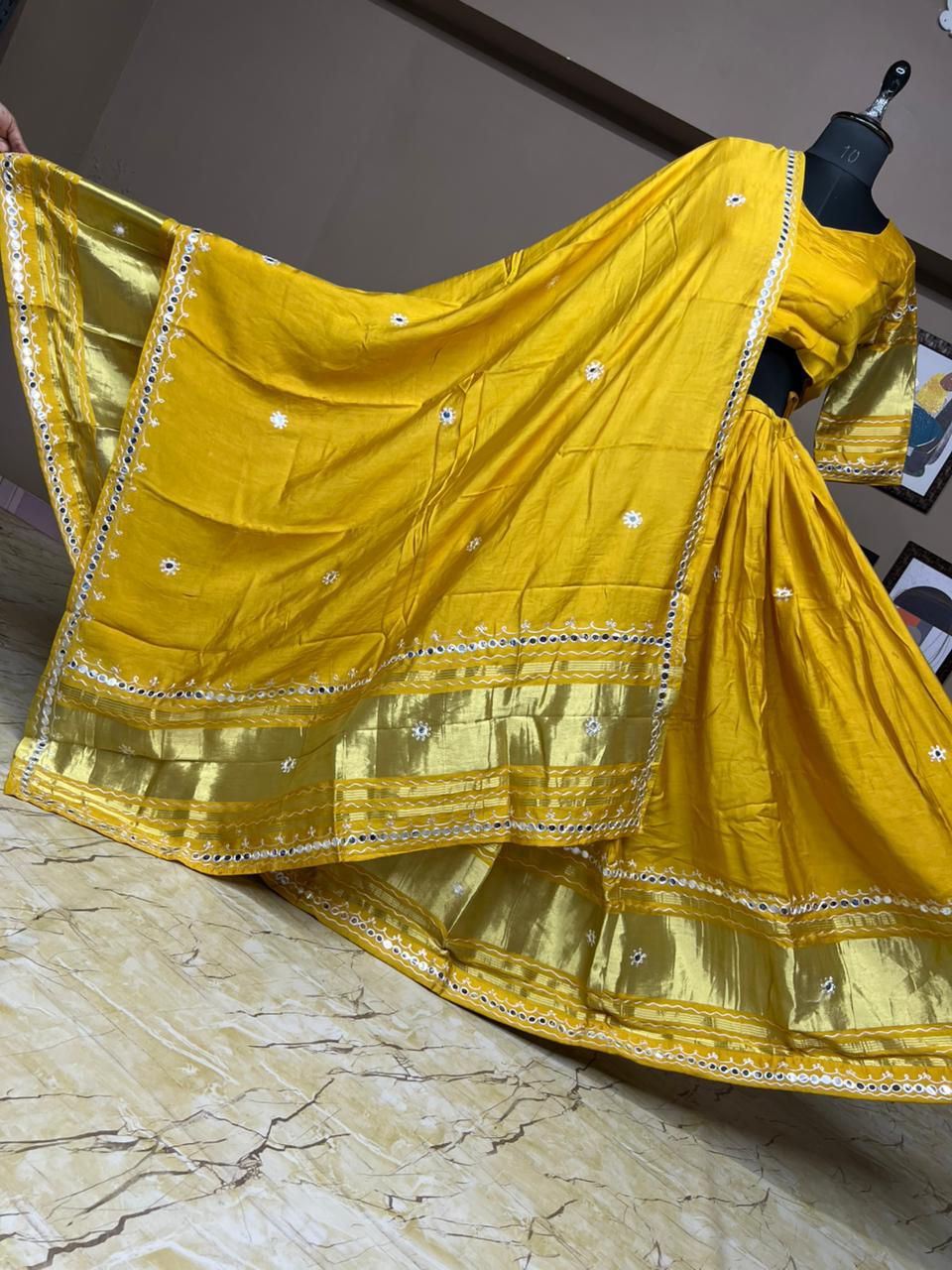 Yellow saree with gold border on a mannequin against a neutral background