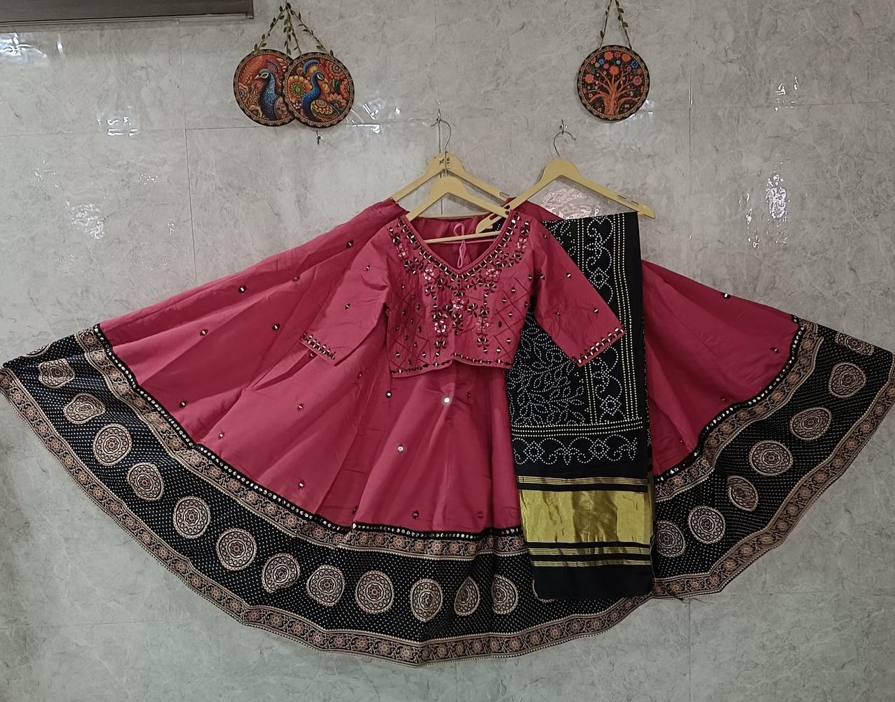 Pink and black traditional outfit with jewelry on a hanger against a tiled wall.
