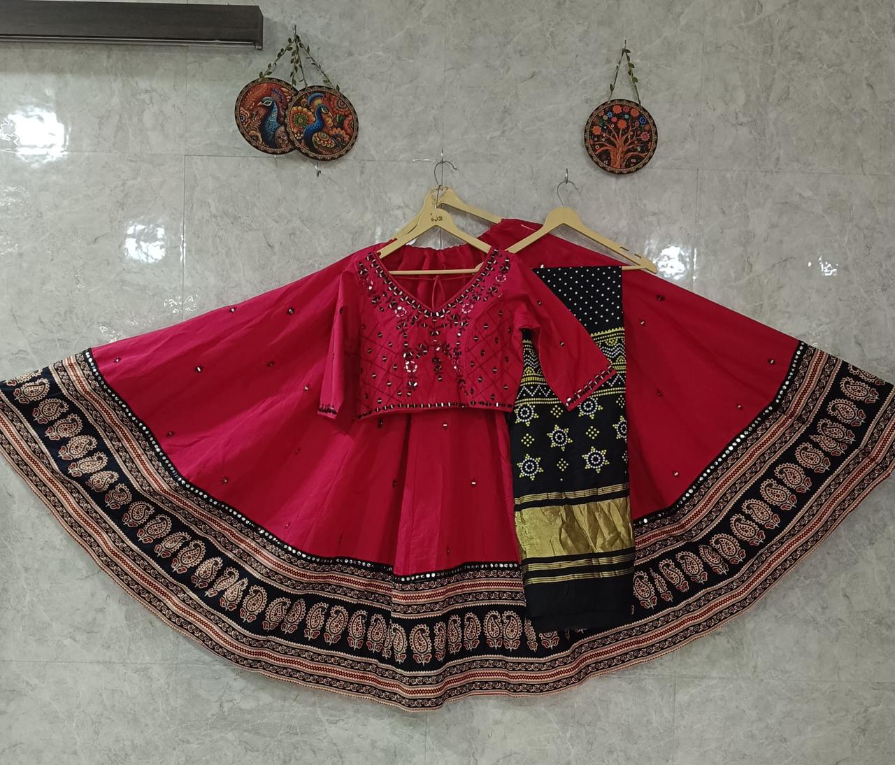 Traditional outfit with pink blouse and black and gold skirt on hangers against a light gray wall.