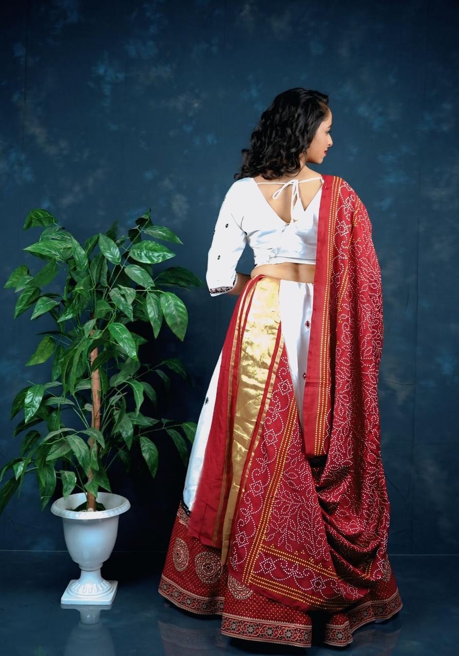 Woman in a white blouse and red saree standing next to a plant against a dark blue background