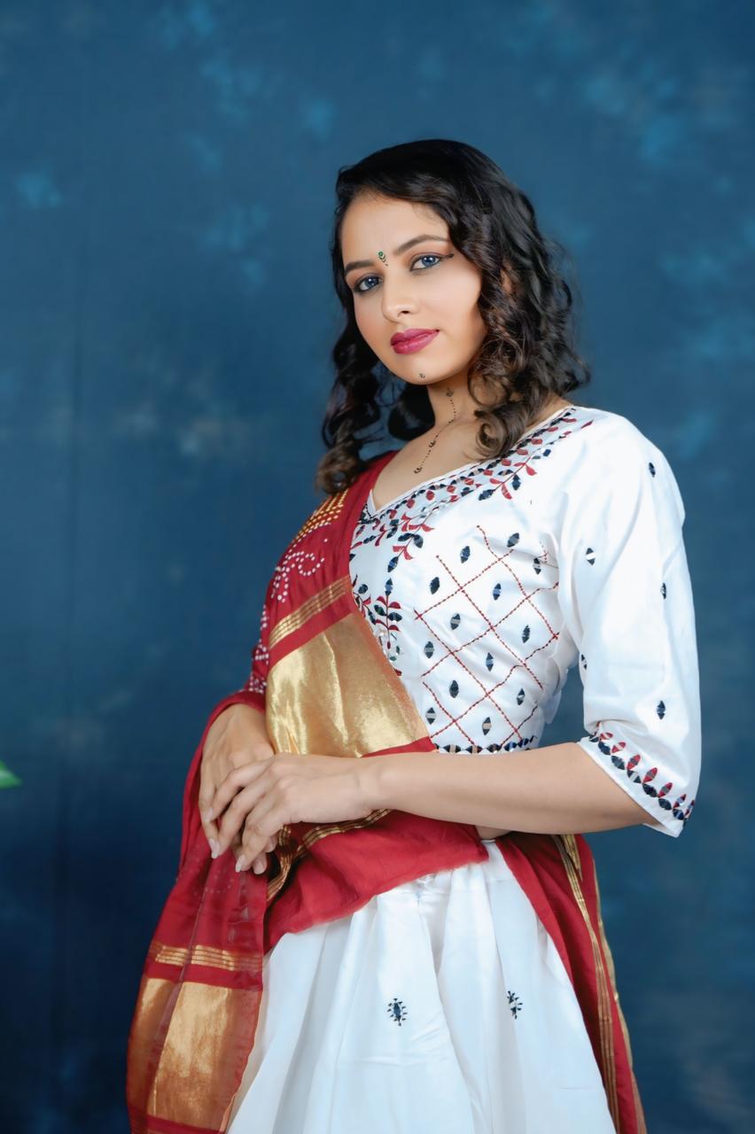 Woman wearing a traditional outfit with a white blouse and red saree against a blue background