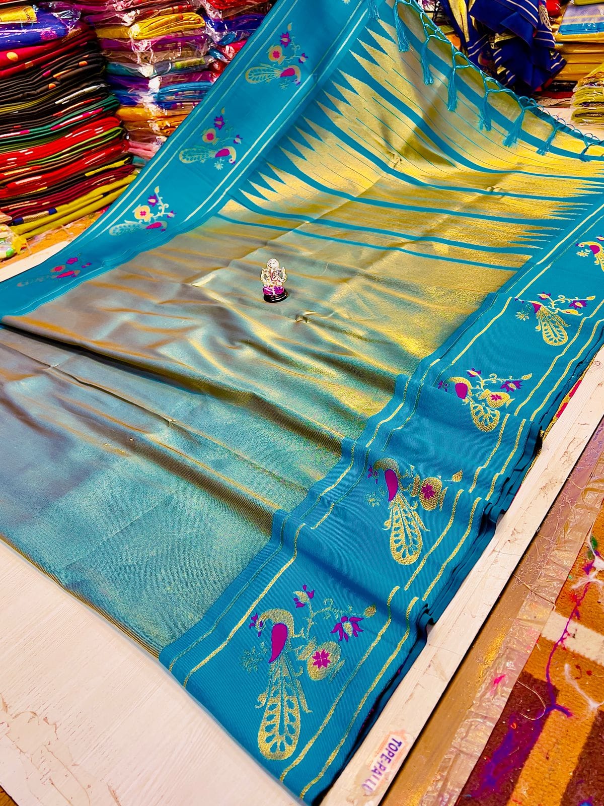 Blue saree with peacock designs on a table with colorful fabric in the background