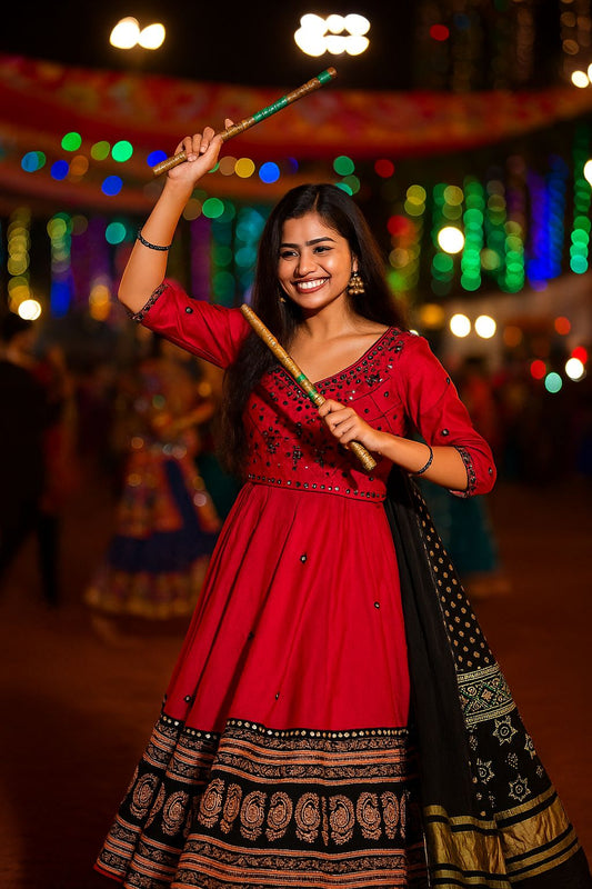Woman in a red and black traditional outfit holding a stick with colorful lights in the background